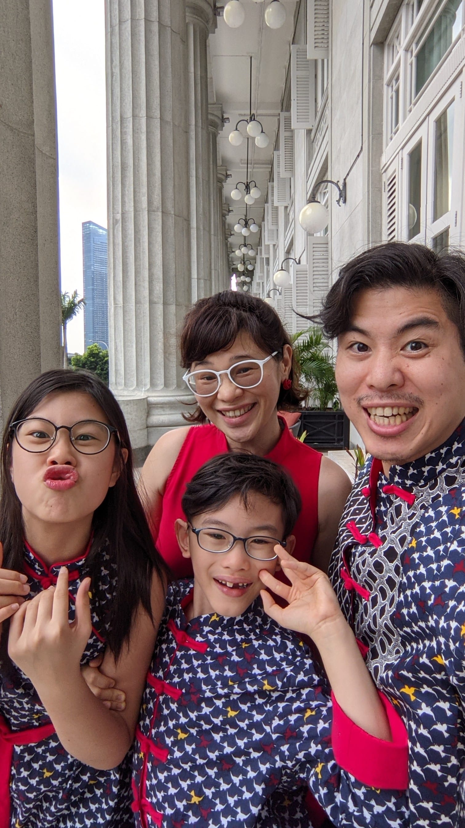 A family of four in matching traditional outfits pose playfully in a colonial-style building with tall stone columns.
